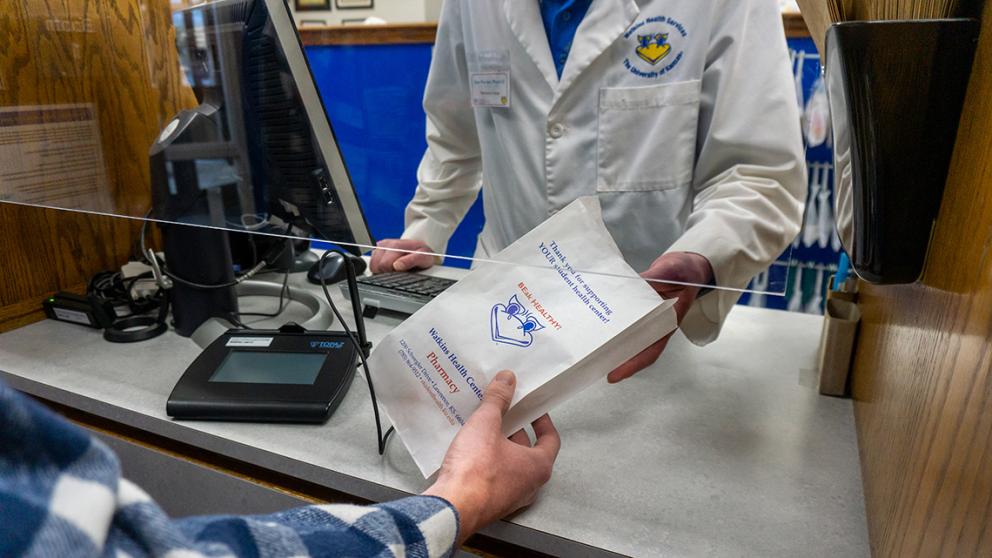 Close up of a Watkins pharmacist handing a prescription bag to a customer